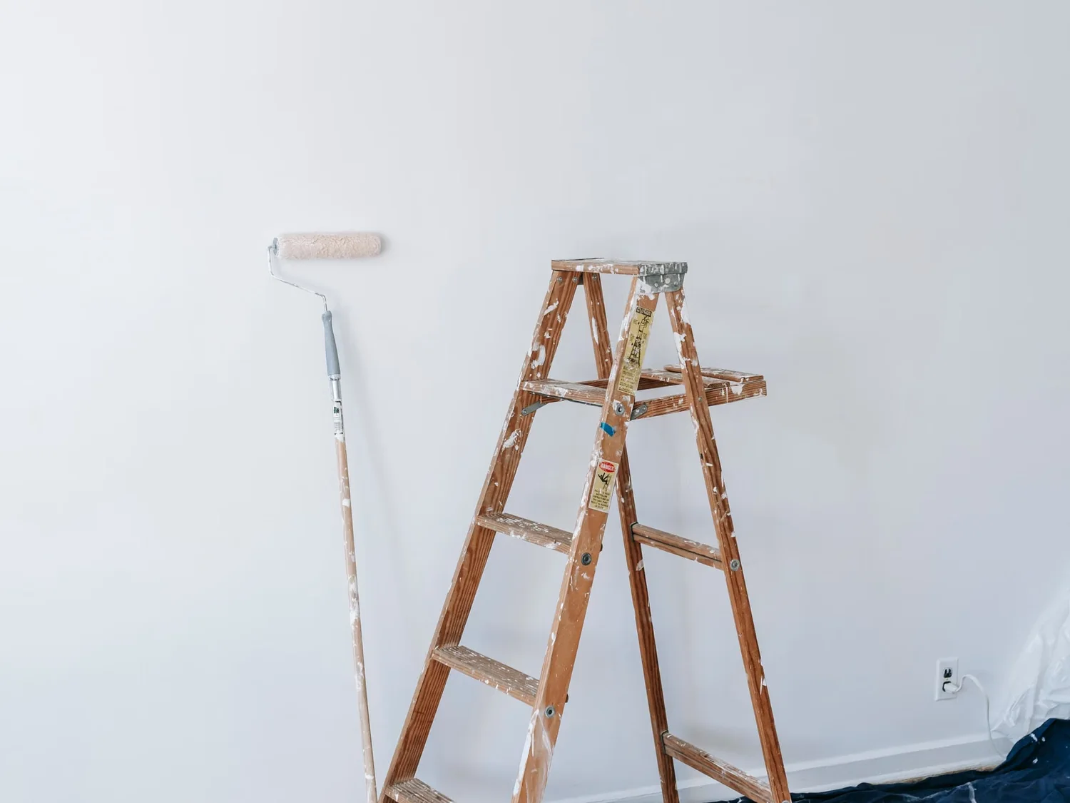 Pièce vide préparée avant peinture, escabeau et sol protégé par une bâche.